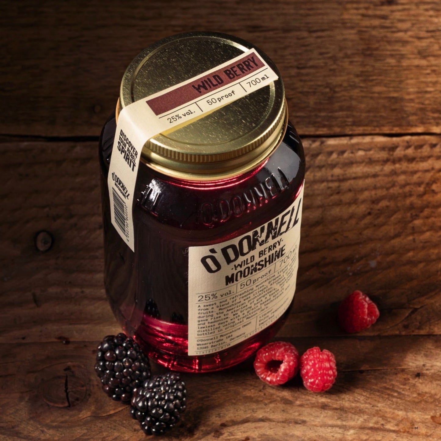 A glass jar of O’Donnell Moonshine Wild Berry with a gold lid and cream label, styled on a rustic wooden surface with blackberries and raspberries.