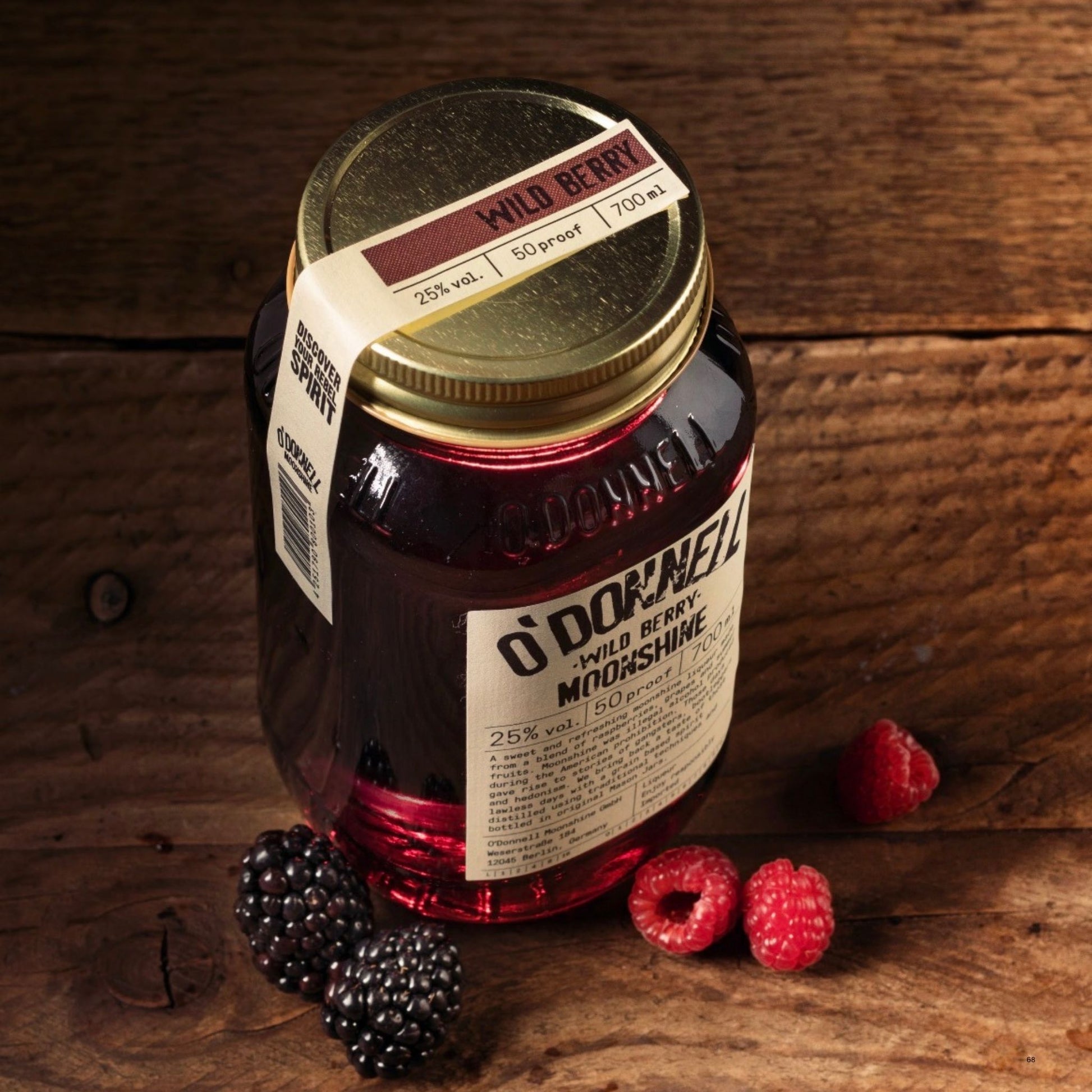 A glass jar of O’Donnell Moonshine Wild Berry with a gold lid and cream label, styled on a rustic wooden surface with blackberries and raspberries.