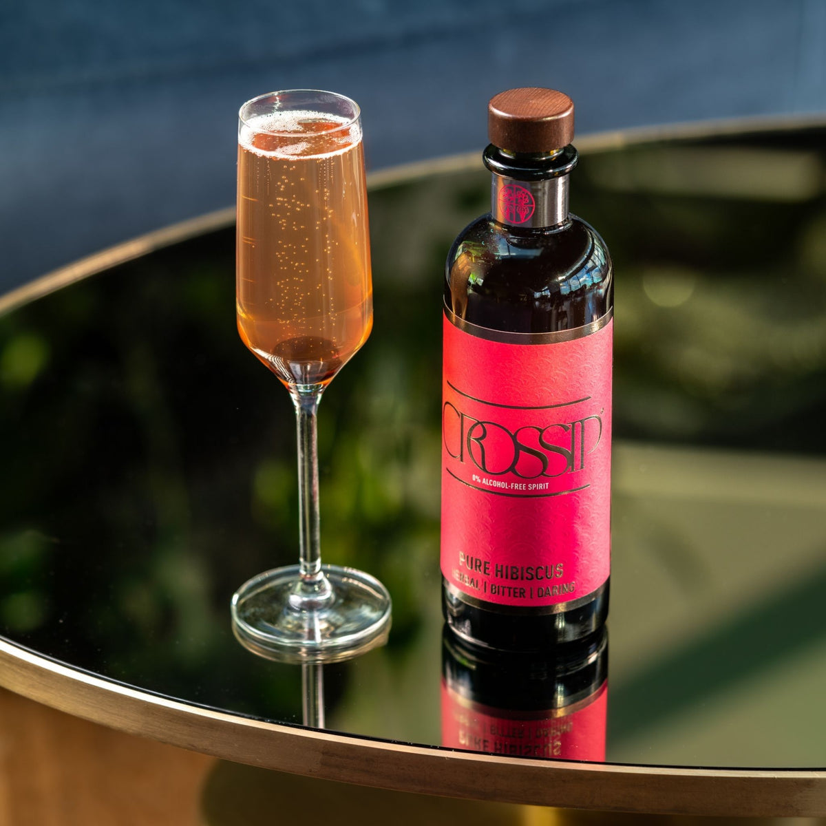 A bottle of CROSSIP Pure Hibiscus sparkling drink with a pink label and a filled champagne flute on a reflective dark table.